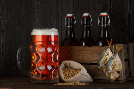 Glass of beer on table with wooden crate full of bottles, bag with beer barley and salty dried fishの写真素材