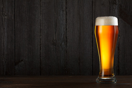 Glass of beer on wooden table, dark background with copy space