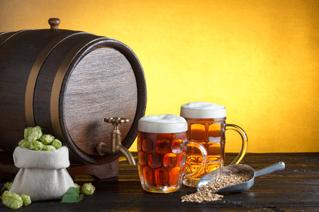 Vintage beer barrel with two beer glasses and bag full of fresh hops, with metal scoop with barley on wooden table still life, copy spaceの写真素材