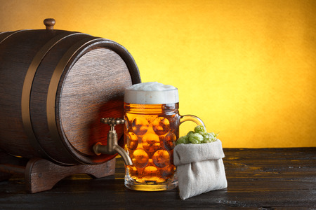 Vintage beer barrel with huge glass of beer and burlap bag with fresh hops on wooden table still lifeの写真素材