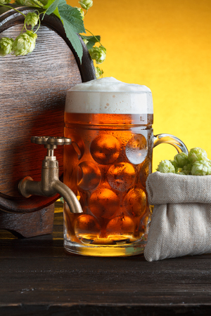 Wooden beer barrel with fresh hop cones and glass of beer on table close upの写真素材