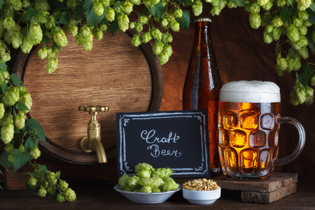 Craft bottled and unbottled beer with barrel, barley and fresh hops for brewing still-lifeの写真素材