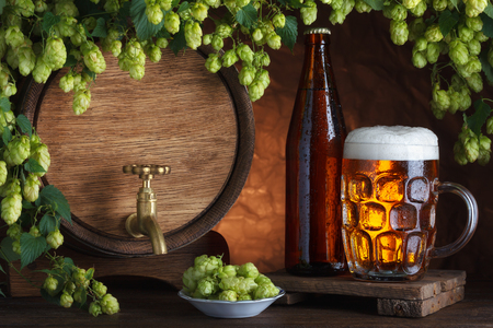 Bottled and unbottled beer with barrel and fresh hops for brewing still-lifeの写真素材