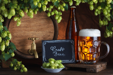 Bottled and unbottled beer with barrel and fresh hops for brewing still-lifeの写真素材