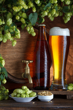 Bottled and unbottled beer with barrel, barley and fresh hops for brewing still-lifeの写真素材