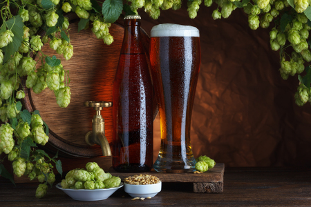 Bottled and unbottled beer with barrel, barley and fresh hops for brewing still-lifeの写真素材