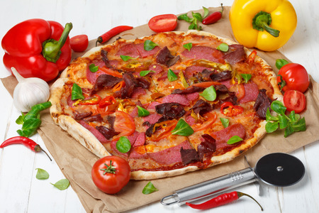 Piiza with a lot of ingredients and pizza cutter knife on wooden table still-lifeの写真素材