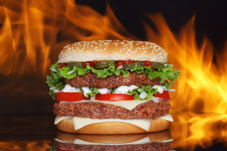Big hamburger on dark background with reflection and real fire on backdropの写真素材