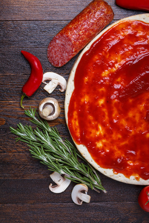 Pizza dough with sauce and different ingredients for cookingの写真素材