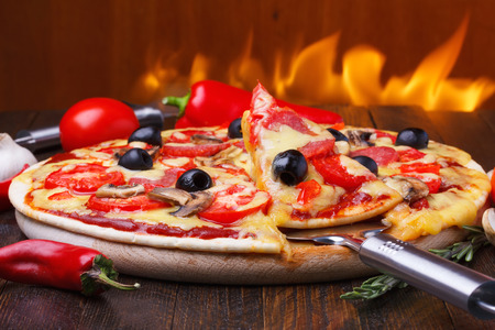 Baked hot pizza with one slice on lifter with fire on backgroundの写真素材