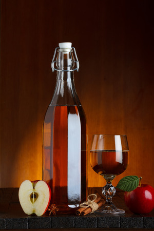 Bottle and glass of apple cider with sliced apple on wooden table with cinnamon and anise starの写真素材