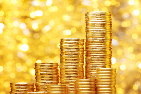 Sparkling new golden coins stacks on bright light glowing bokeh background, business finance wealth and success conceptの写真素材