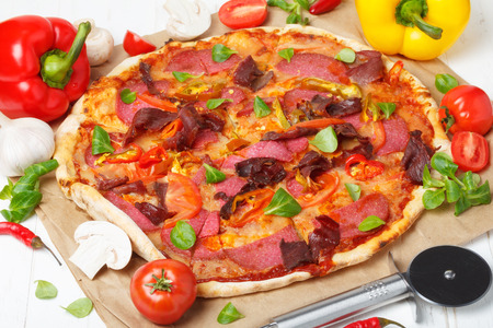 Traditional home made pizza with ham and salami on white kitchen wooden tableの写真素材