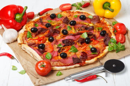 Pizza with salami, ham and black olives on wooden tableの写真素材