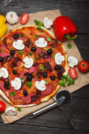Hot italian pizza on dark wooden table with ingredients and cutterの写真素材