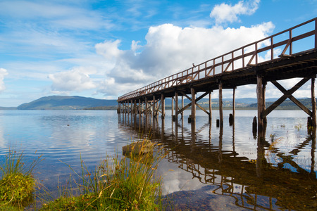 Mountain lake with wooden pier and bird on it at sunny dayの写真素材
