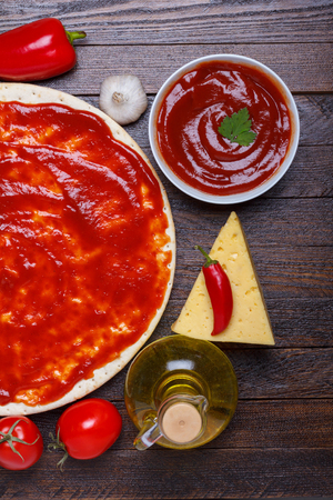 Pizza dough with sauce and different ingredients for cooking on wooden tableの写真素材