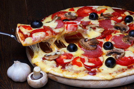 Lifted pizzza slice with melting cheese on dark wooden tableの写真素材