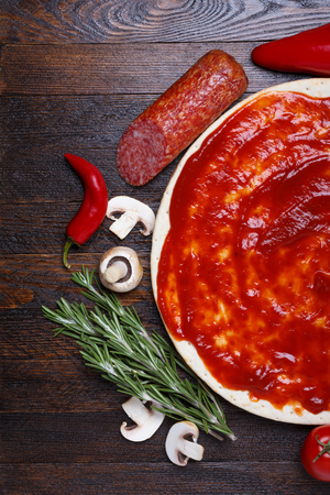 Pizza dough with sauce and different ingredients for cooking on wooden tableの写真素材