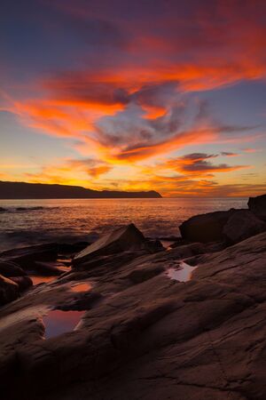 Sunset on ocean beach with reflection in small pools in rockの写真素材