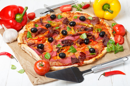Pizza with vegetables and salami on wooden table with lifter and cutter knifeの写真素材