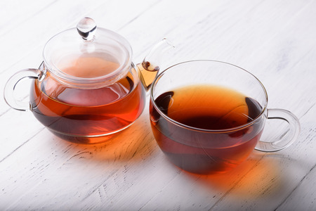 Glass teapot and cup with hot black tea on white wooden tableの写真素材