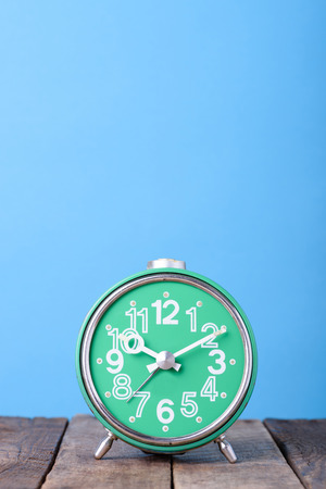 Old green retro clock on wooden table with blue background still life with copy spaceの写真素材