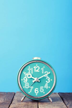 Blue retro clock on wooden table, vertical still life with copy space, vintage tonedの写真素材