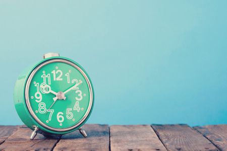 Vintage alarm clock on wooden table with blue background, retro tonedの写真素材