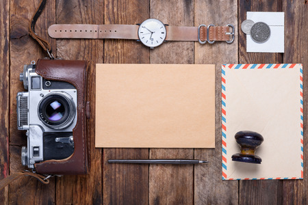 Blank card with envelope and vintage camera, stamps, watch, ink pen on wooden table still lifeの写真素材