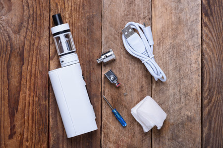 Electronic cigarette with coils, atomizer and heads on wooden table still life