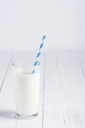 Glass of milk with paper striped straw on white wooden tableの写真素材