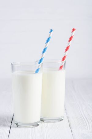 Two glasses of milk with blue and red stripped paper straws on white wooden table still lifeの写真素材