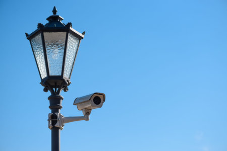 CCTV surveillance camera mounted on vintage street lantern over blue sky background