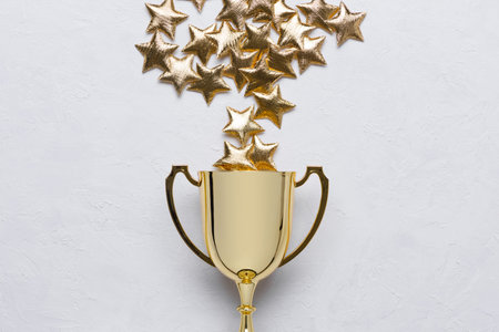 Golden winner trophy cup with golden stars on white textured background