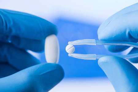 Small pill in tweezers in scientist hands, new medicine research conceptの写真素材
