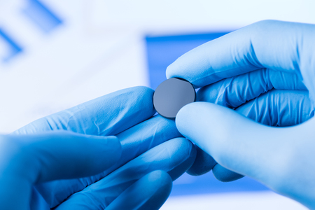 Scientist hold in hands in protective gloves small round piece of glass, new type of glass or plastic with new properties research conceptの写真素材