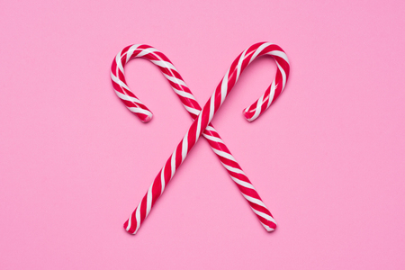 Shiny red and white traditional candy canes crossed on pink backgroundの写真素材