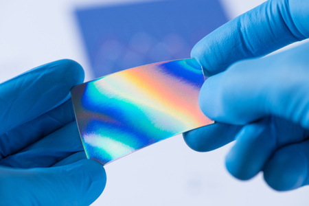 Piece of new type of material or thin coating on plastic with improved properties in laboratory in scientist hands, iridescent and pressure sensitiveの写真素材