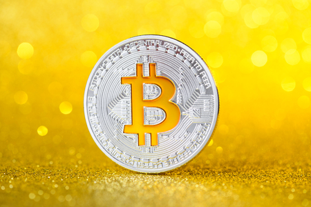 Shiny silver bitcoin coin. Golden bitcoin symbol on golden shiny glitter backgroundの写真素材