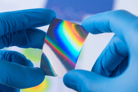 Piece of new type of material or thin coating on plastic with improved properties in laboratory in scientist hands, iridescent and pressure sensitiveの写真素材