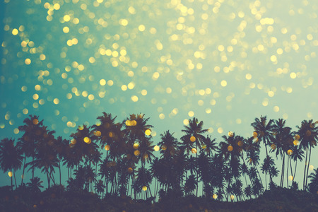Palm trees on tropical beach, vintage toned and retro color stylized with shiny golden party bokeh backgroundの写真素材