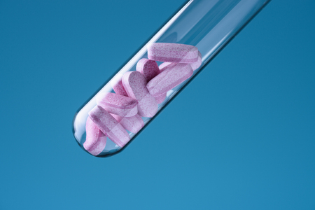 Laboratory glass test tube filled with pink pills on blue backround. Medicine research concept.の写真素材