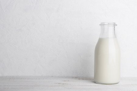 Full glass bottle of milk on white wooden table background with copy spaceの写真素材