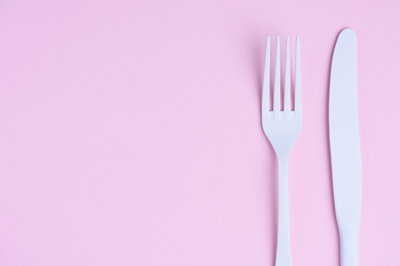 White knife and fork on trendy soft pink pastel paper backgroundの写真素材