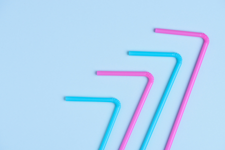 Pink and blue pastel colored drinking cocktail straws on blue paper background with side copy spaceの写真素材
