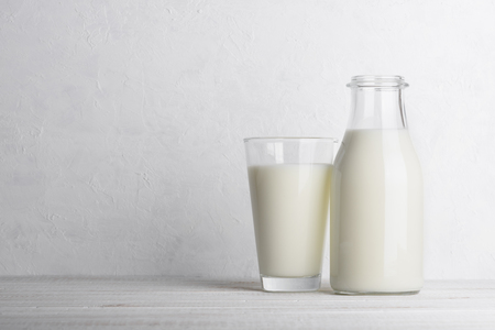 Bottle and glass of milk on white wooden table background with white wall as side copy spaceの写真素材