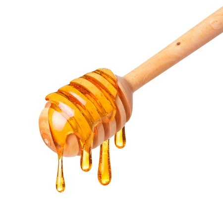 Honey dripping from wooden dipper spoon isolated on white backgroundの写真素材