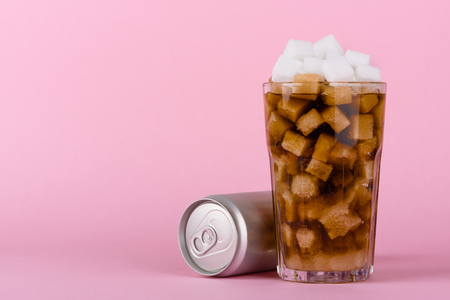 Drinking glass of of lump sugar cubes and soft cola drink with aluminum can on pink pastel background. Unhealthly diet with sweet sugary soft drinks concept.の写真素材