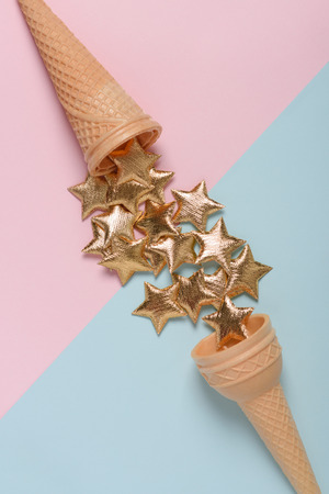 Two ice cream wafer cones with golden stars on blue and pink pastel background top viewの写真素材